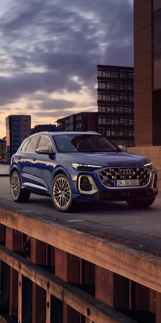 Der SQ5 SUV steht vor der Skyline einer Küstenstadt. Davor befindet sich eine junge, modische Frau. 