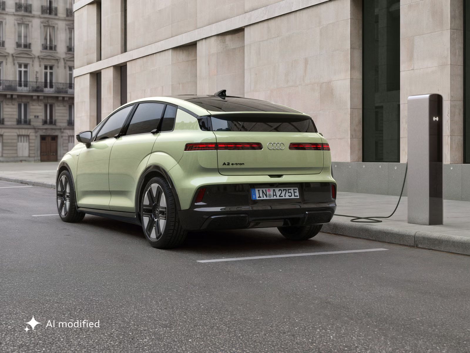 Audi A2 e-tron, odfotené šikmo zozadu, je zaparkované pred modernou budovou. Vozidlo je pripojené k nabíjacej stanici.