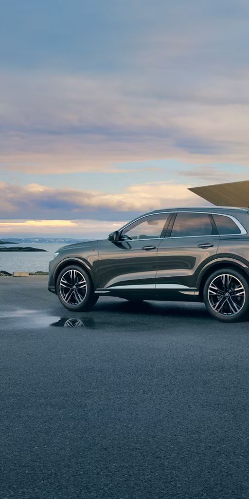 Audi Q5 SUV zaparkované na voľnej ploche pri avantgardnej budove pri pobreží.