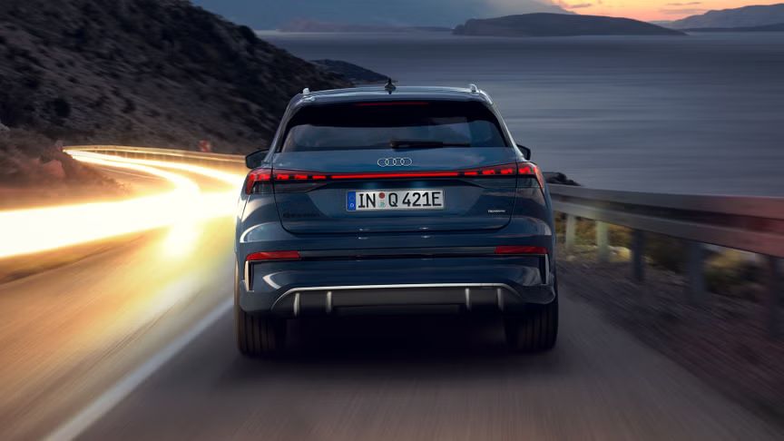 Audi Q4 SUV e-tron zozadu v noci na strmej horskej ceste, vpravo je more. V protismere vidieť svetelné čiary prechádzajúcich vozidiel. 