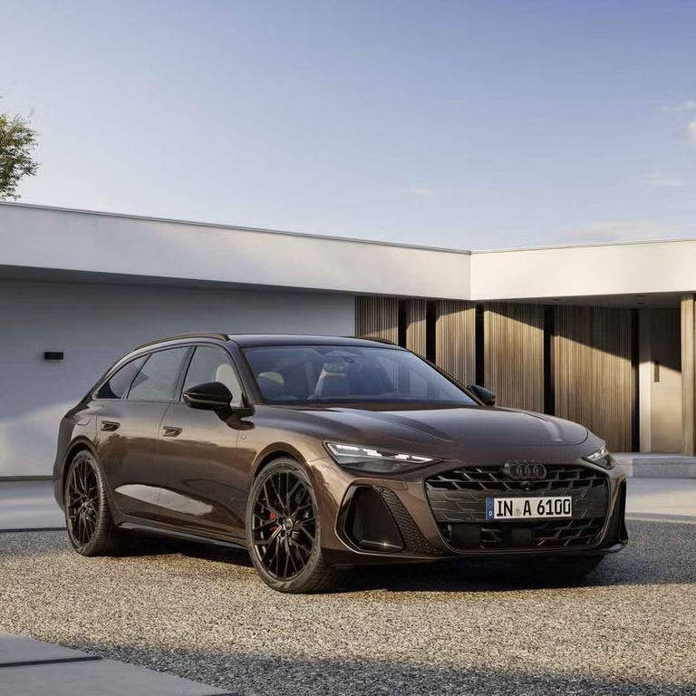 A6 Avant stojí v šikmom čelnom pohľade na štrkovom povrchu pred moderným domom. Predné svetlomety vozidla vytvárajú charakteristický svetelný obrazec.