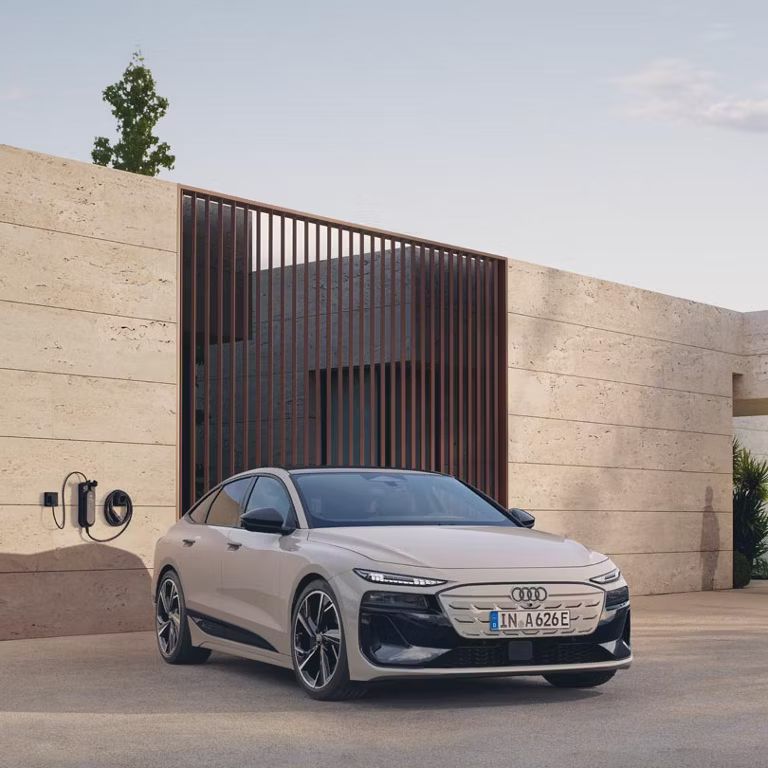 Pohľad na predné pratie Audi A6 Sportback e-tron zaparkovaný pred modernou budovou s kamennou fasádou.