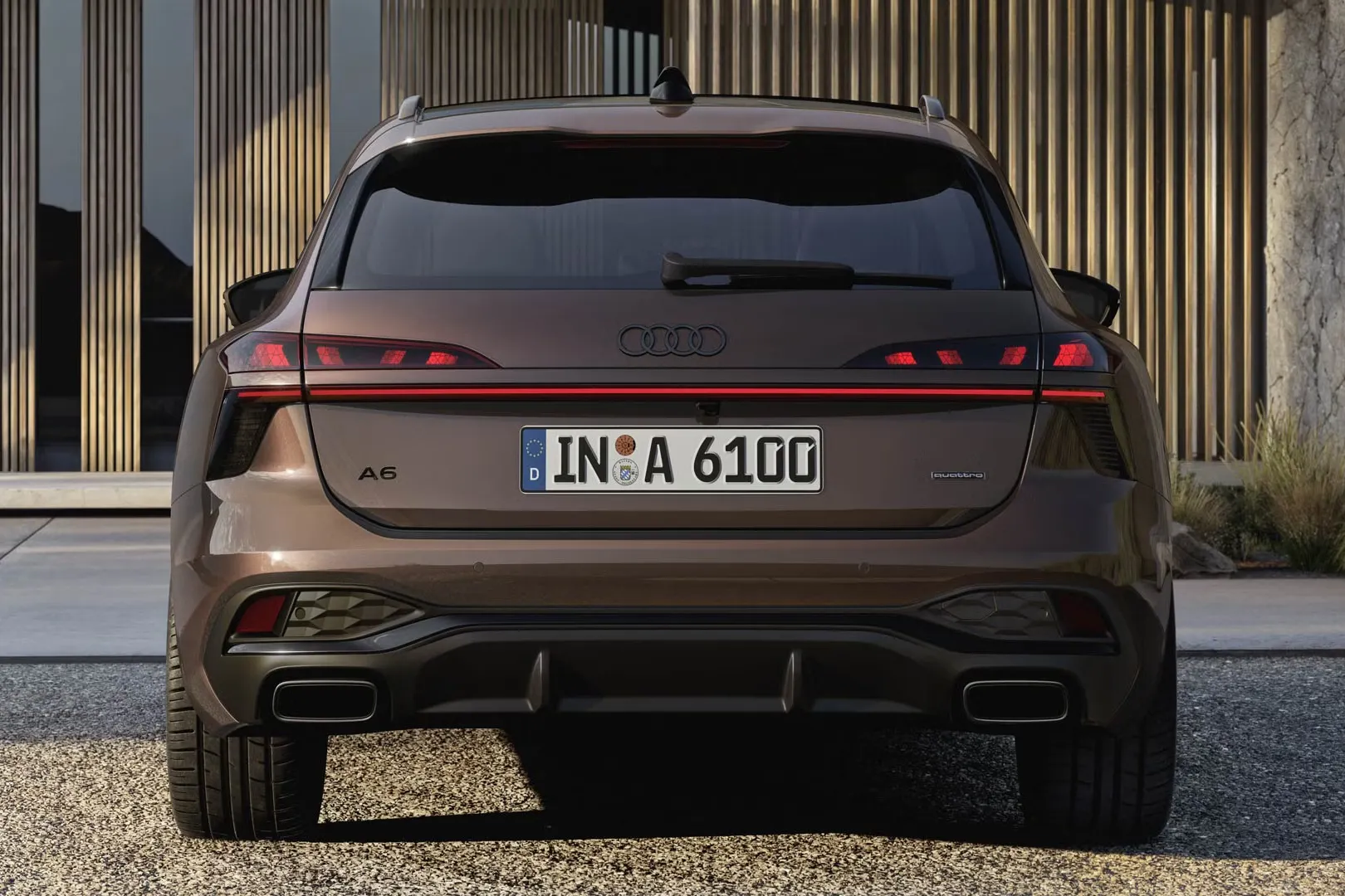 Audi A6 Avant, ktorý stojí na štrkovom povrchu pred fasádou s dreveným obkladom a vysokými oknami.