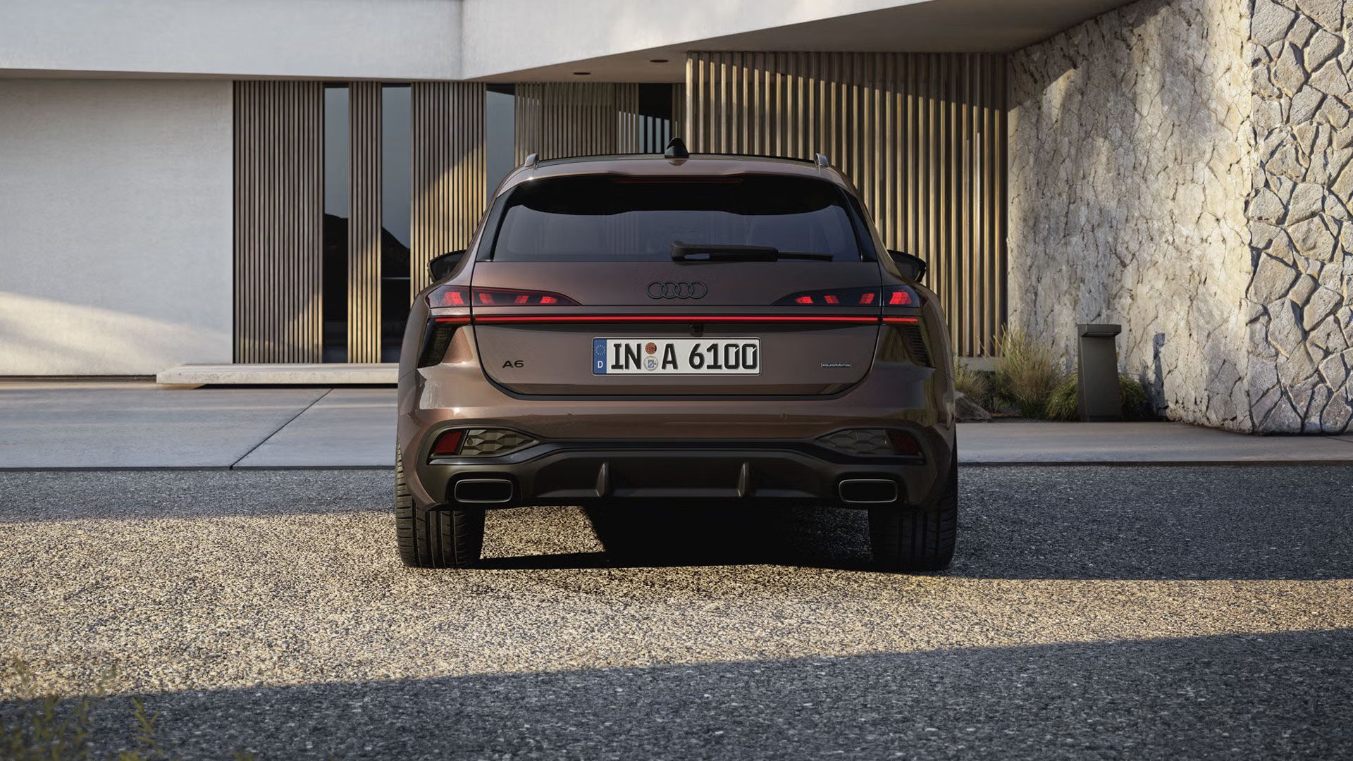 Pohľad na zadné partie Audi A6 Avant, ktorý stojí na štrkovom povrchu pred fasádou s dreveným obkladom a vysokými oknami.