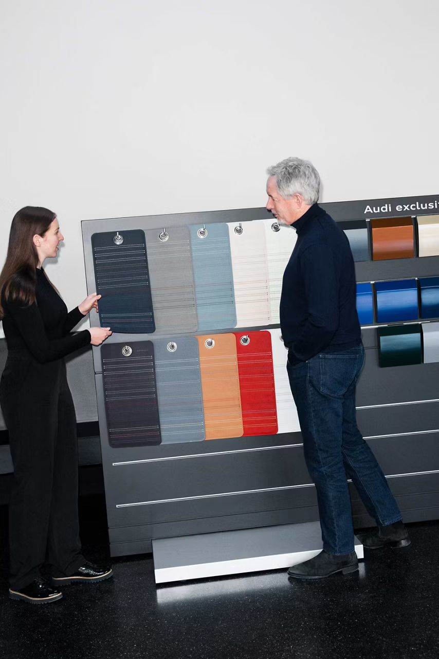 Muž a žena stoja pred prezentačným panelom, na ktorom visia rôzne farby kože a karosérie a diskutujú o nich.