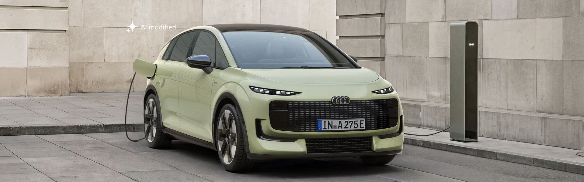 Audi A2 e-tron je zaparkované pred modernou budovou. Vozidlo je pripojené k nabíjacej stanici.