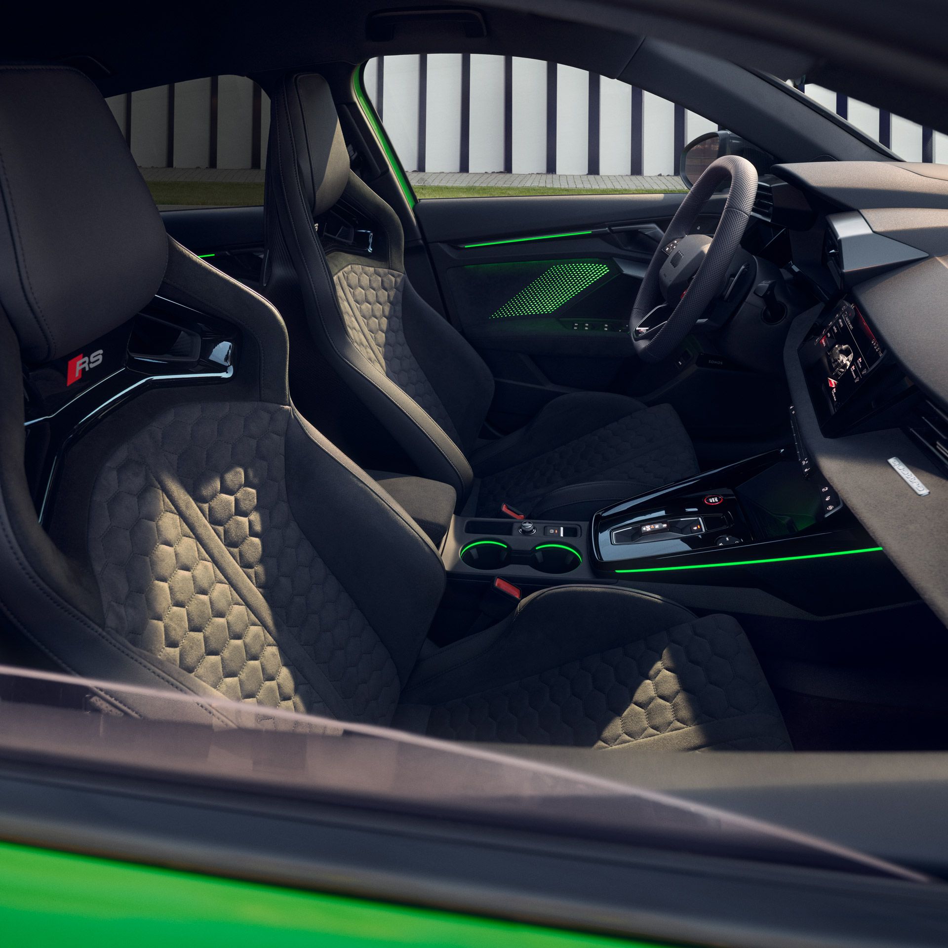 Pohľad do interiéru Audi RS 3 Limuzína cez okno spolujazdca. Vidieť môžeme športové, anatomické sedadla s voštinovým prešívaním, športový multifunkčný volant, palubnú dosku, ale aj exkluzívne výplne dverí.