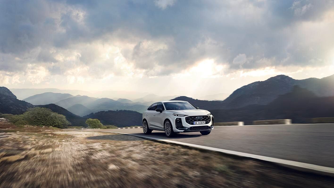 Audi Q3 Sportback e-hybrid jazdí po horskej ceste pod zamračenou oblohou. Krajina je rozľahlá a ponúka pohľad na hory a údolia.