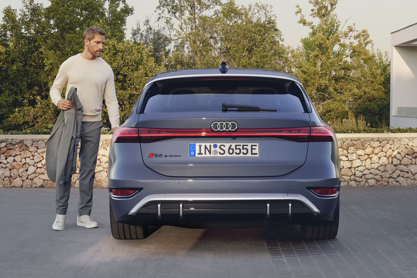 Audi S6 Avant e-tron zaparkované pred moderným domom. Elegantné oblečený muž stojí pri vozidle.