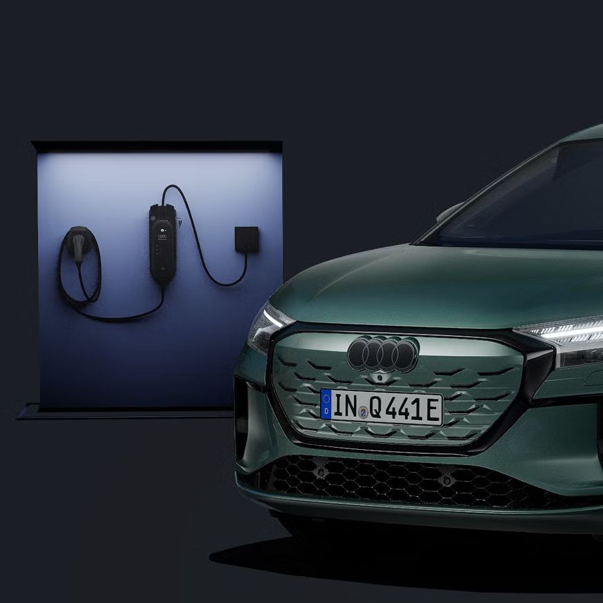 Q4 Sportback e-tron zobrazený z čelného pohľadu na tmavom pozadí, za ním moderná nabíjacie stanica.