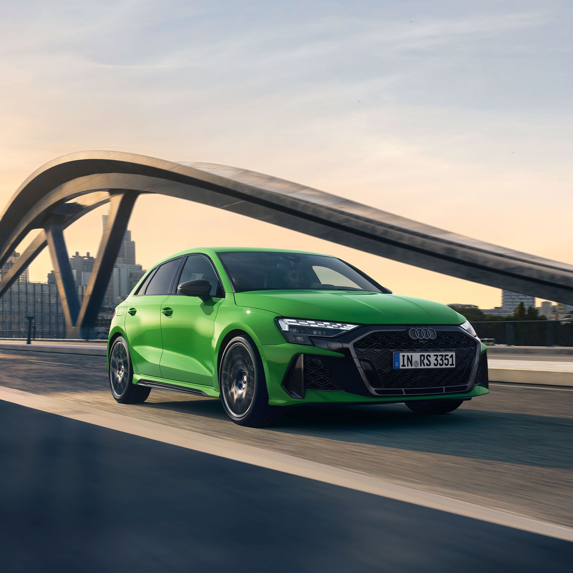Zelené Audi RS3 Sportback z bočného pohľadu počas dynamickej jazdy po moste. 