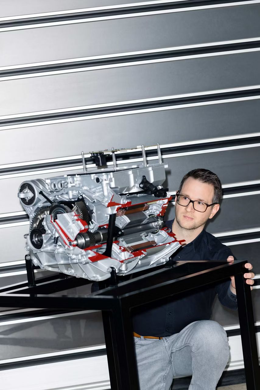 Muž sa pozerá na model elektrického pohonu, ktorý je položený na čiernom kovovom podstavci.