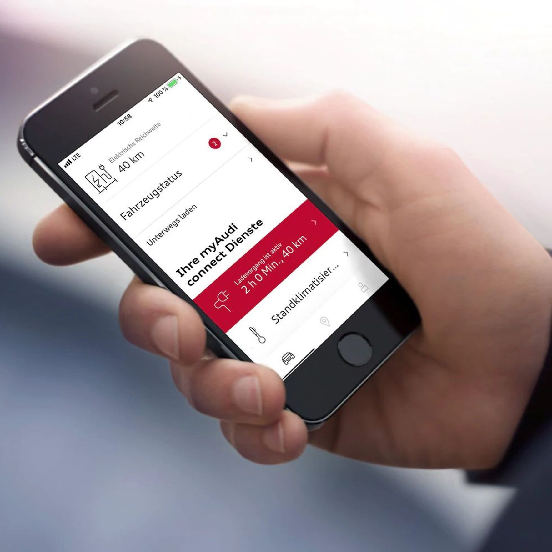 Osoba drží v ruke mobilný telefón, na ktorom je zobrazená aplikácia "myAudi connect". Na obrazovke sú zobrazené informácie o stave vozidla a jeho poslednom pripojení k internetu. Telefon má čiernu farbu.