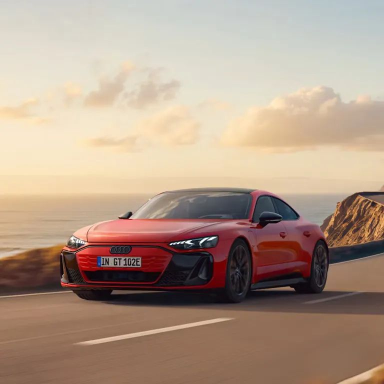 Audi e-tron GT quattro počas jazdy na ceste na útesoch s výhľadom na more pri slnečnom dni.