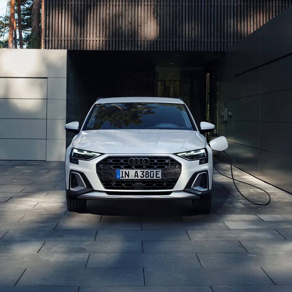 Biele Audi A3 allstreet TFSI e zaparkované pri modernej vile s domácou nabíjacou stanicou. Vozidlo je napojené a nabíja sa.