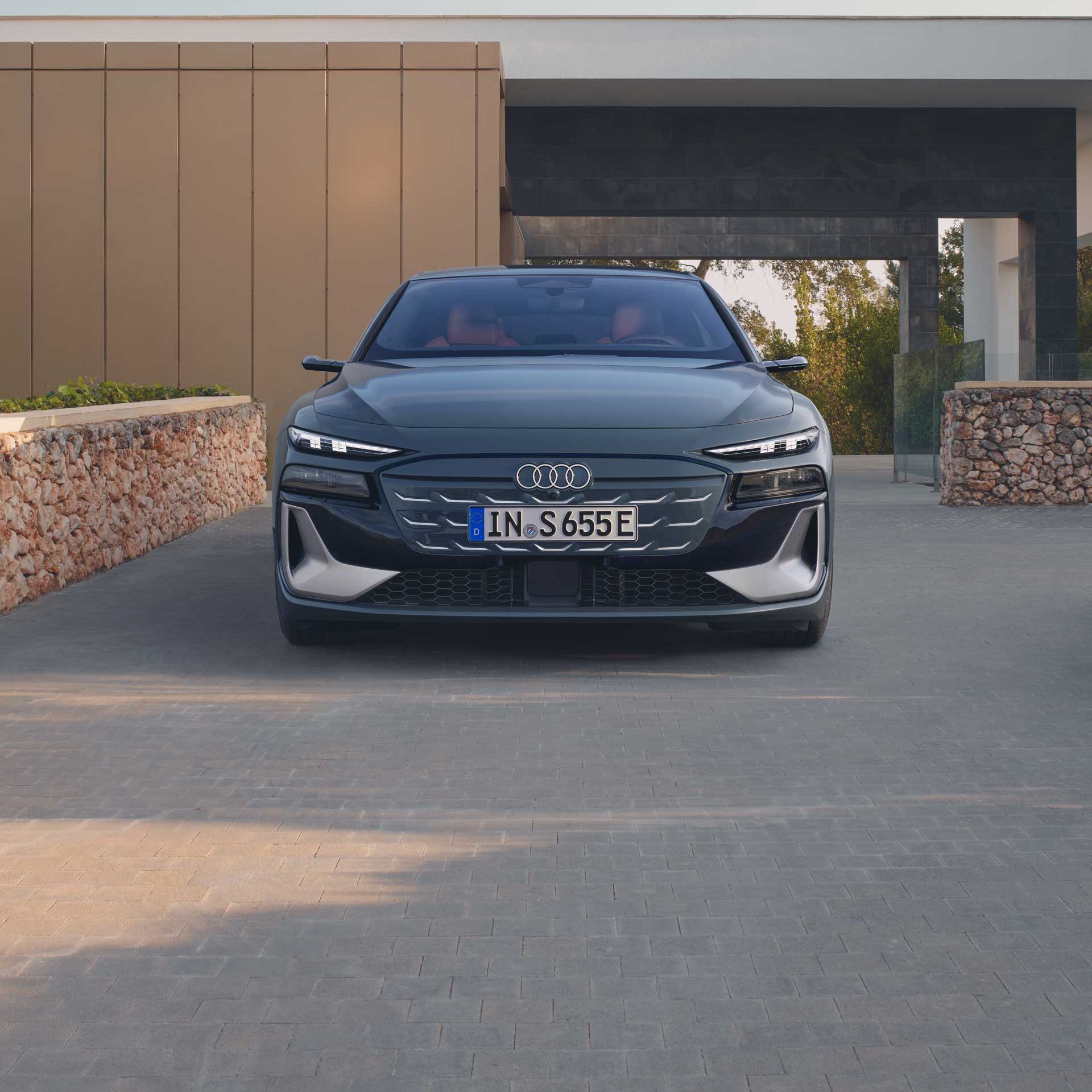 Pohľad na predné partie Audi S6 Avant e-tron, ktorý je zaparkovaný pred modernou rodinnou vilou.