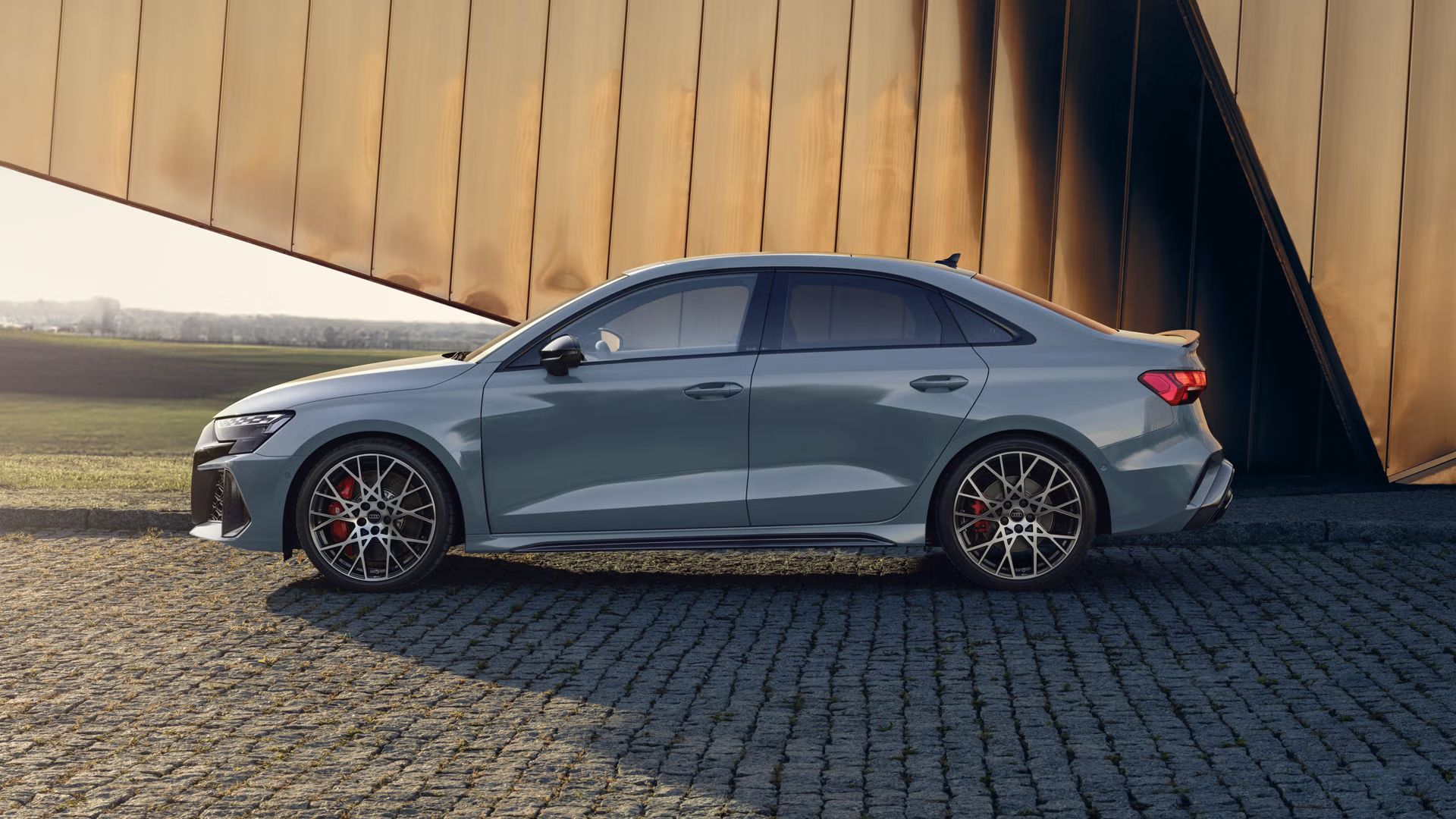 Audi RS 3 Limuzína zaparkované na dlažobných kockách, v pozadí vidieť modernú budovu.