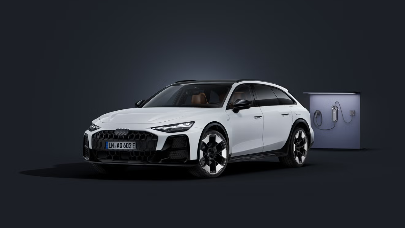 Audi A6 allroad e-hybrid zachytené z čelného uhla na tmavom pozadí. Vedľa neho stojí moderná nabíjacia stanica.