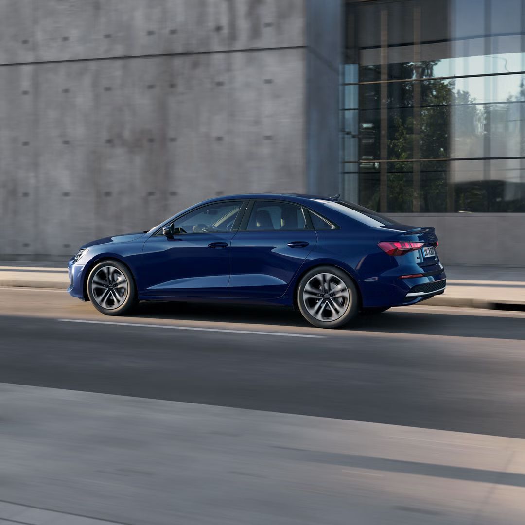 Audi A3 Limuzína z boku na mestskej ulici. Za ním stojí moderná budova s betónovým vzhľadom.