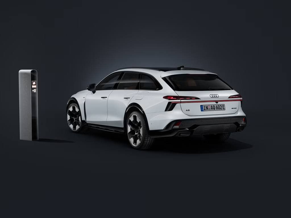 Audi A6 allroad e-hybrid zachytené zozadu pod uhlom na tmavom pozadí. Vedľa neho stojí moderná nabíjacia stanica.