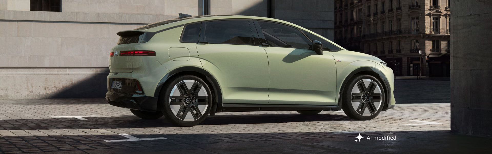 Audi A2 e-tron, odfotené z boku, je zaparkované pred modernou budovou v meste. Slnečné svetlo vytvára scenériu s tieňmi. 