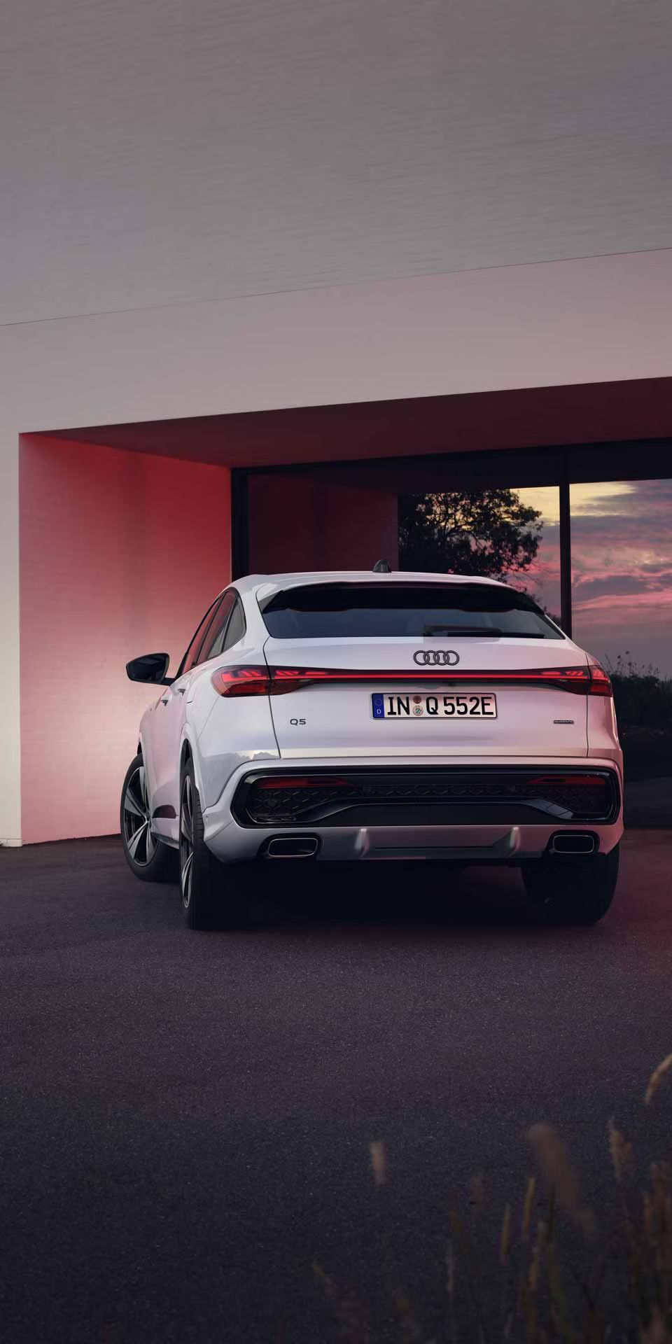 Heckansicht des Q5 Sportback e-hybrid, welcher vor bodentiefen Fenstern eines Hauses steht und diese mit seinen Scheinwerfern anleuchtet.