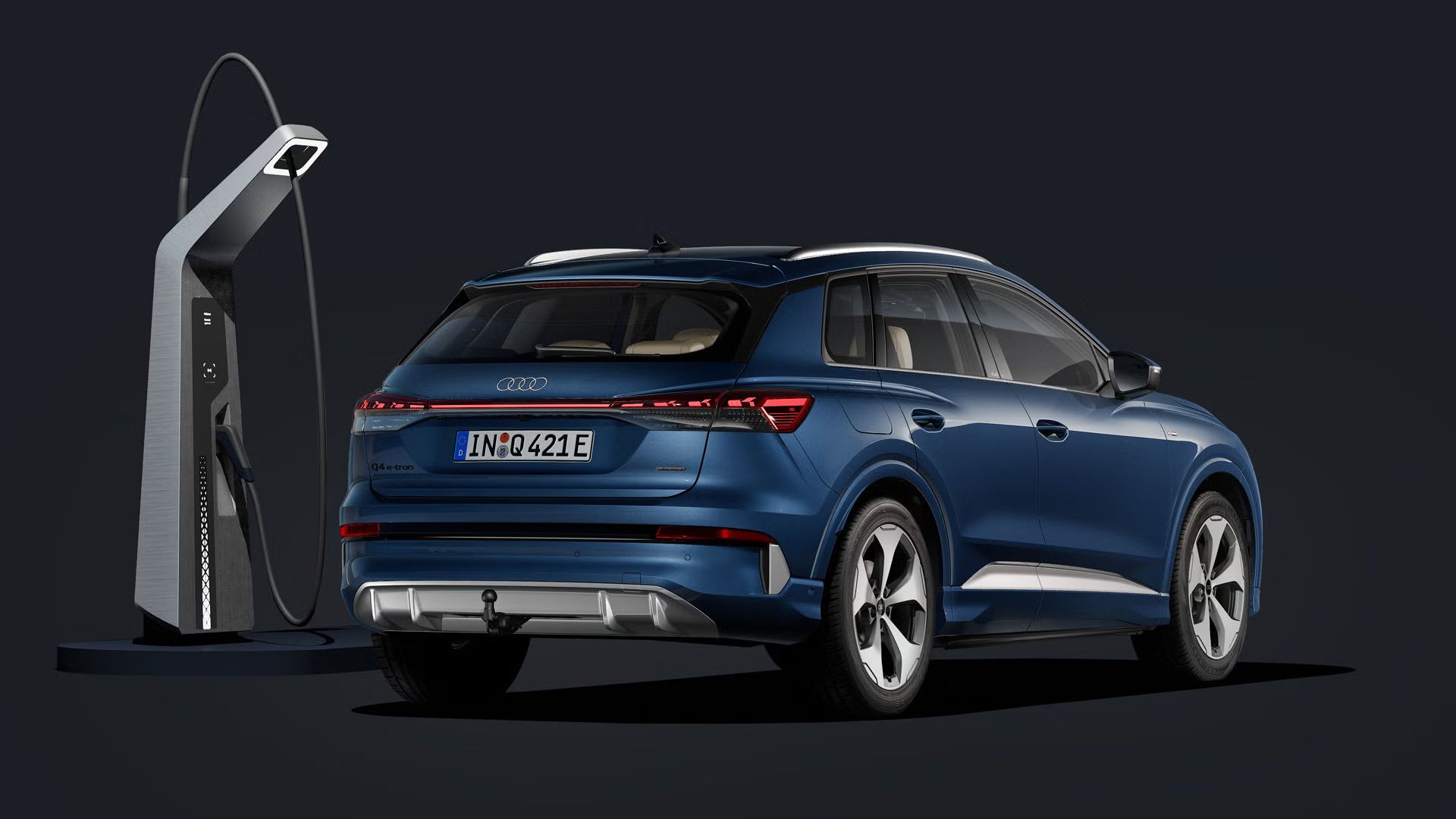 Q4 SUV e-tron šikmo zozadu na tmavom pozadí. S modernou nabíjacou stanicou z ľavej strany vozidla.