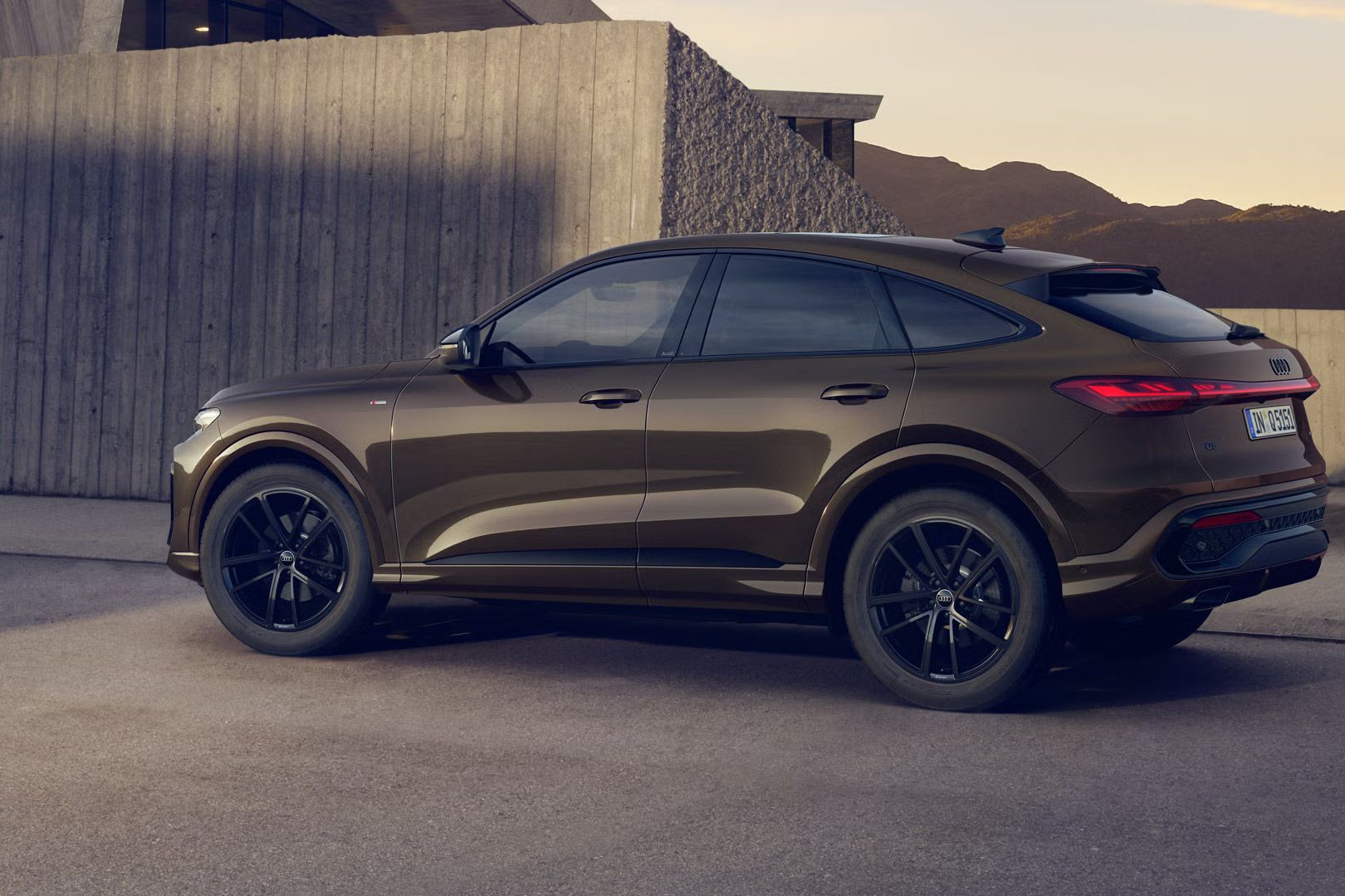 Q5 Sportback s individuálnym lakovaním v odtieni Teak hnedá metalíza stojí pred budovou. V pozadí sú viditeľné hory.