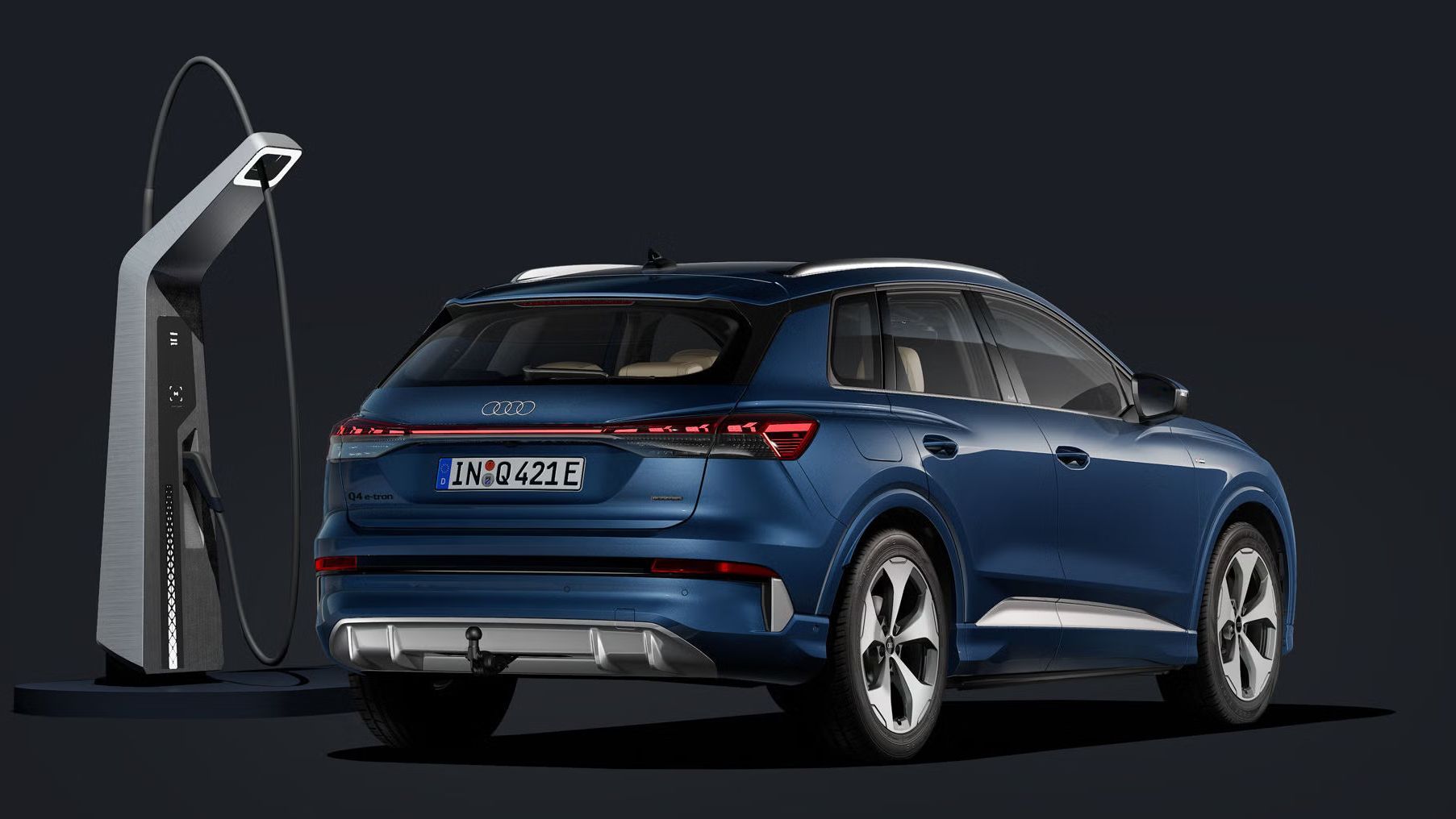 Q4 SUV e-tron šikmo zozadu na tmavom pozadí. S modernou nabíjacou stanicou z ľavej strany vozidla.