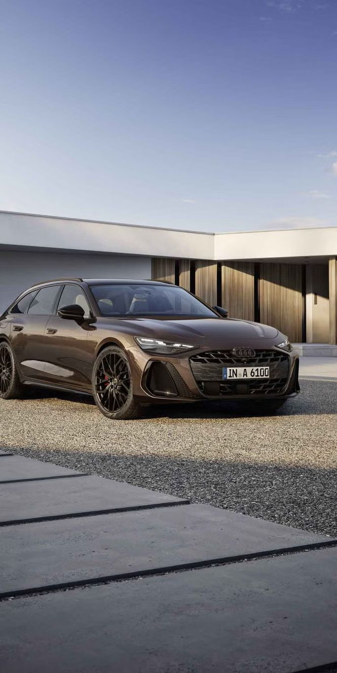 Der A6 Avant steht im schrägen Frontprofil auf einer Kiesfläche vor einem modernen Haus. Die Frontscheinwerfer des Fahrzeugs zeigen eine Lichtsignatur.