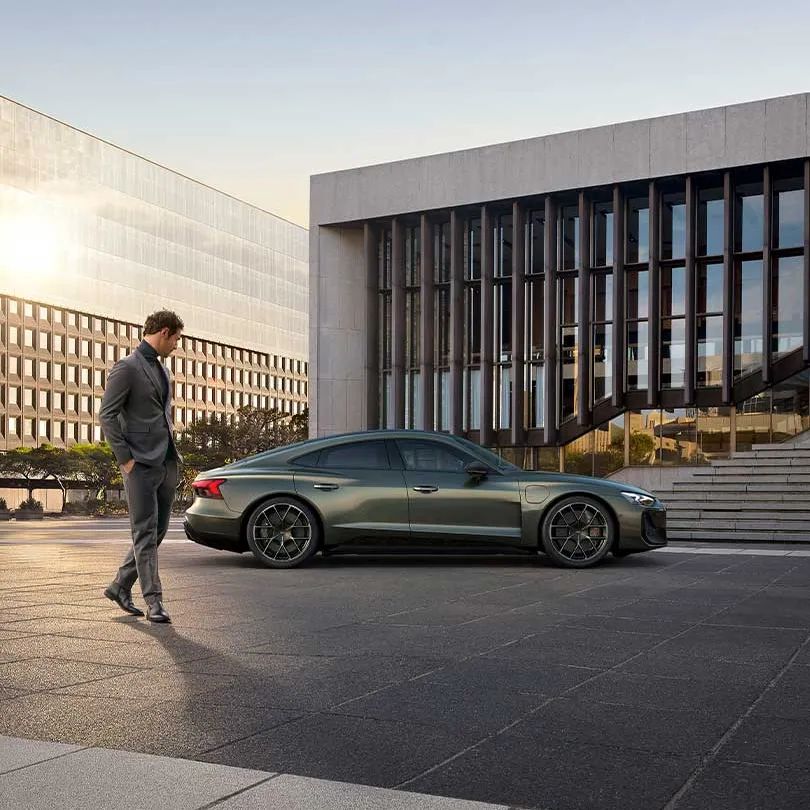 Audi RS e-tron GT Performance zaparkovaný pred verejnou budovou inštitúcie. Okolo vozidla prechádza elegantne oblečený muž a obzerá si ho.