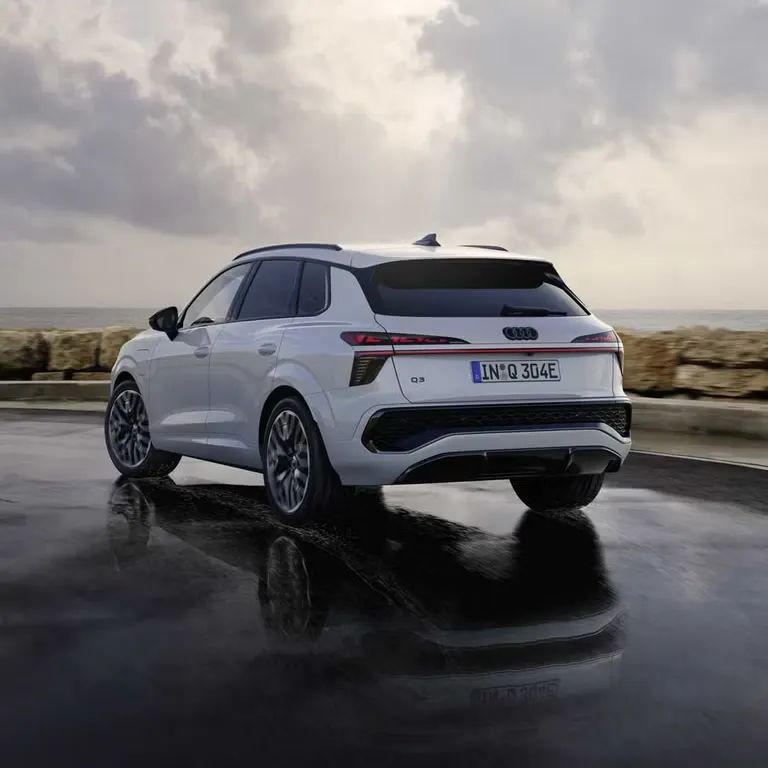 Audi Q3 SUV e-hybrid stojí na mokrej ceste pri pobreží. Atmosféru dotvára zatiahnuté počasie.