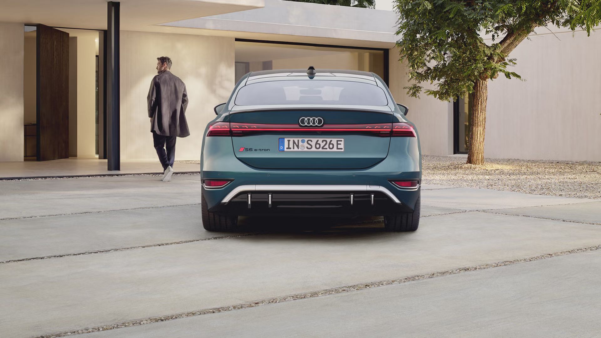 S6 Sportback e-tron v zadnom profile. Vozidlo je otočené smerom k vstupnej časti modernej budovy. Pred autom stojí mladý muž, ktorý beží smerom k budove.