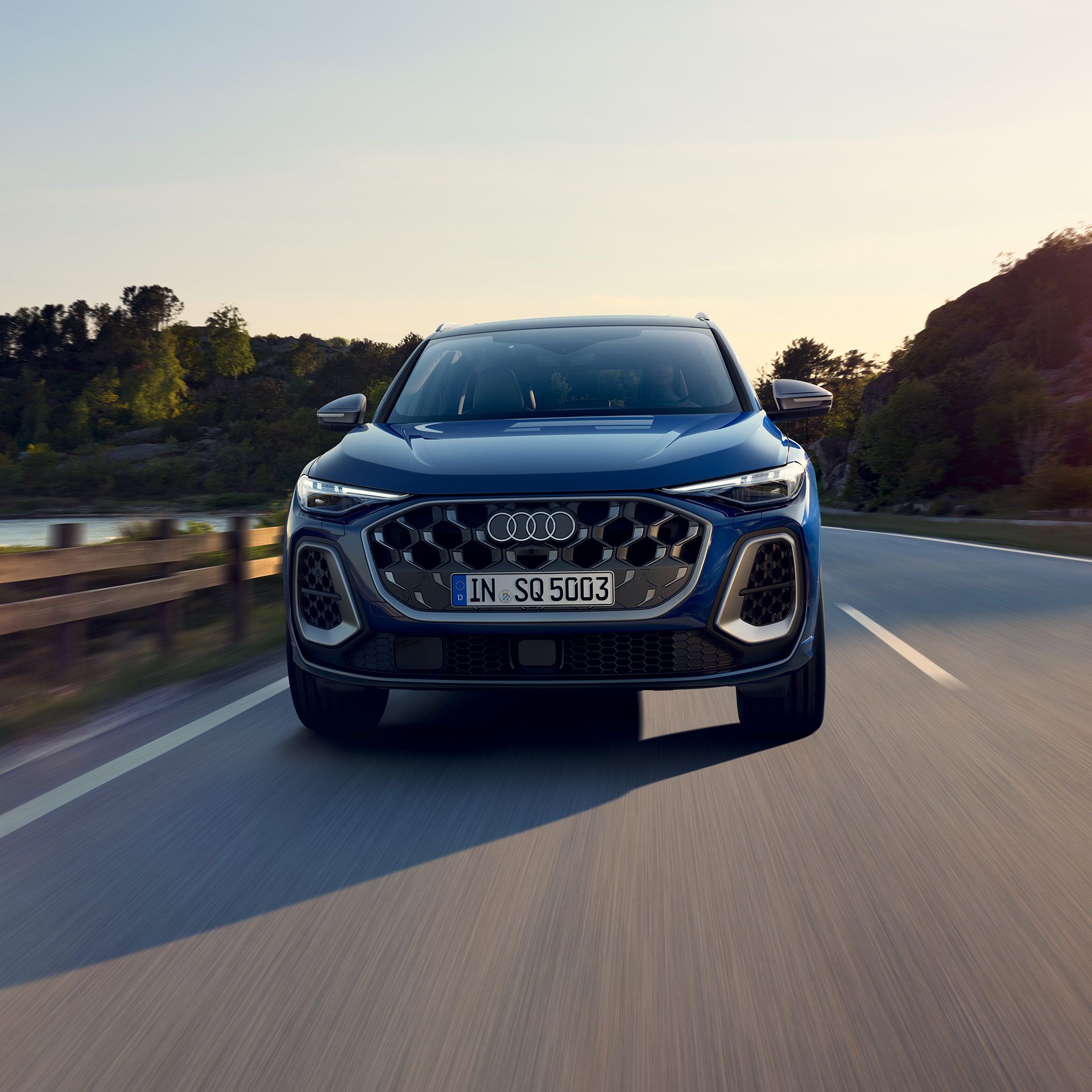 Audi SQ5 SUV počas jazdy po ceste popri pobreží. Za vozidlom je hustá vegetácia a jasná obloha.