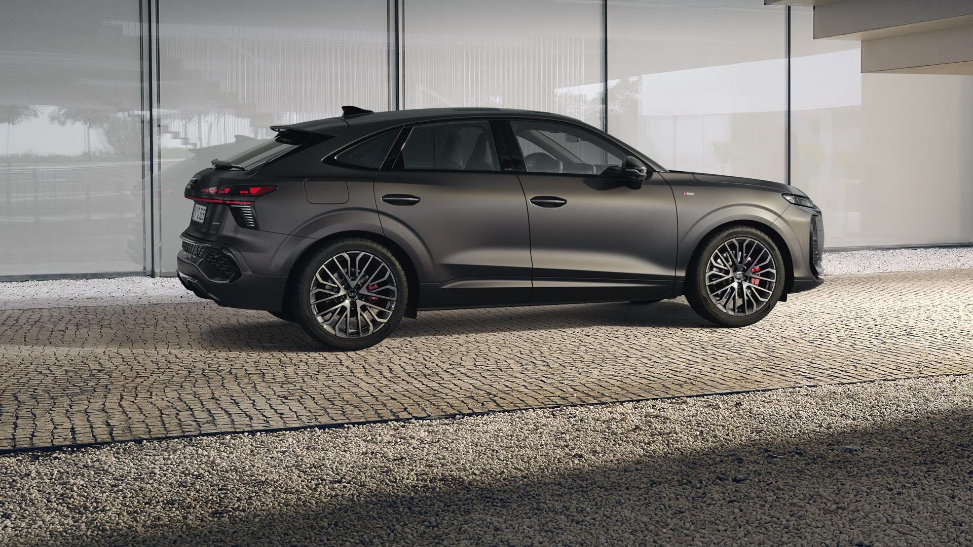 Audi Q3 Sportback je zaparkovaný pod schodiskom budovy na dláždenej ploche..