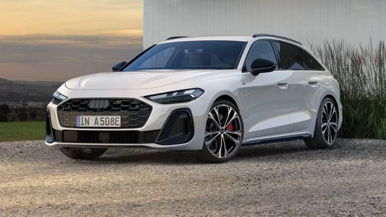 Biele Audi A5 Avant e-hybrid zaparkované na štrkovej ploche pri bielej modernej budove. Za vozidlom je zeleň a v pozadí vidieť mesto.