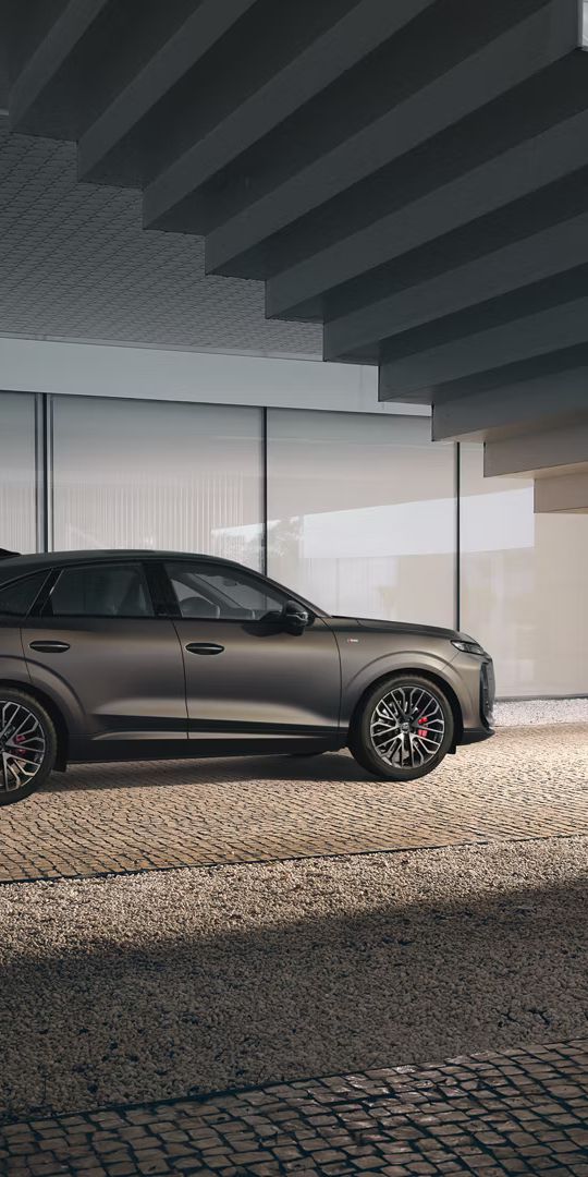Audi Q3 Sportback stojí pod schodmi pri modernej budove. Pohľad zboku ponúka detailnejší náhľad na detaily exteriéru.en Details der Außenseite.