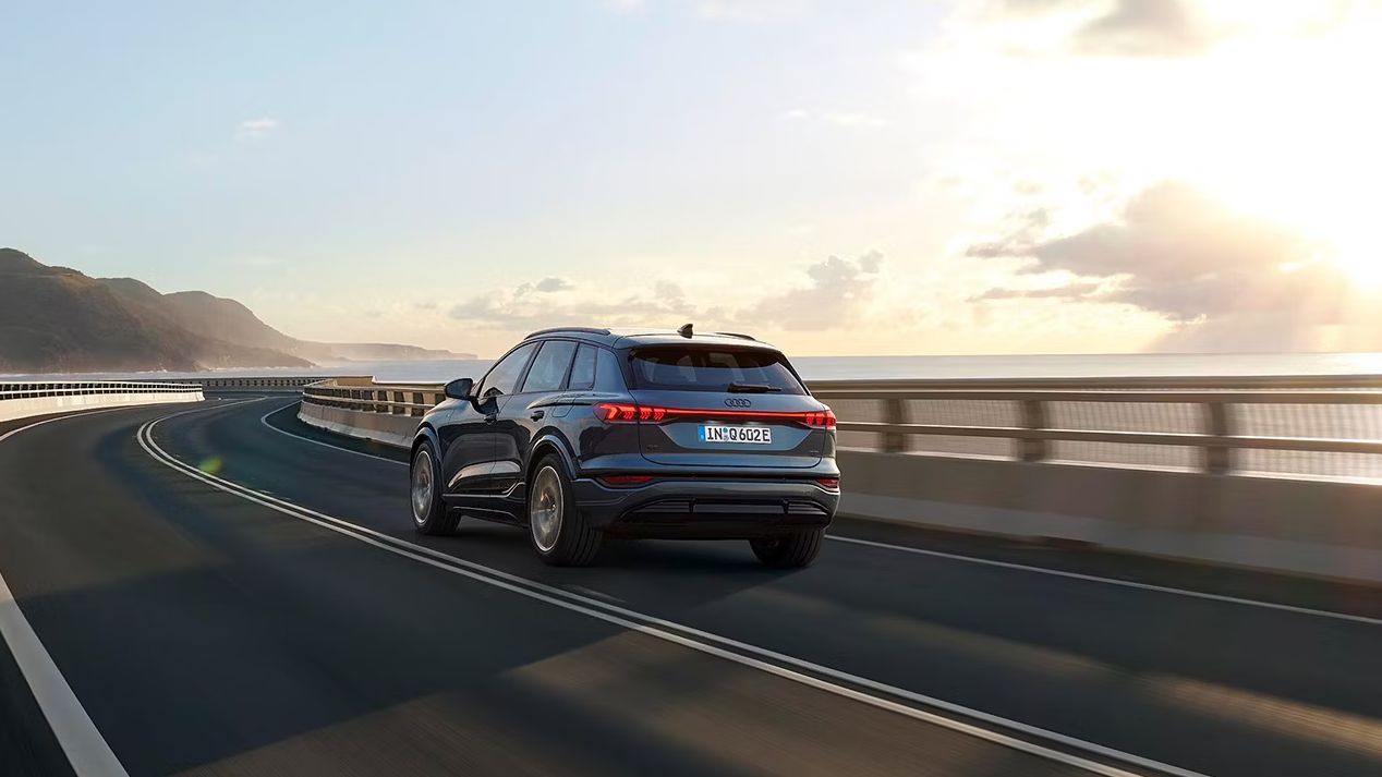 Pohľad na zadné partie Audi Q6 počas dynamickej jazdy po ceste popri pobreží.