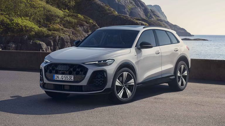 Audi Q5 SUV e-hybrid na parkovisku pri pobreží so skalnatými útesmi.