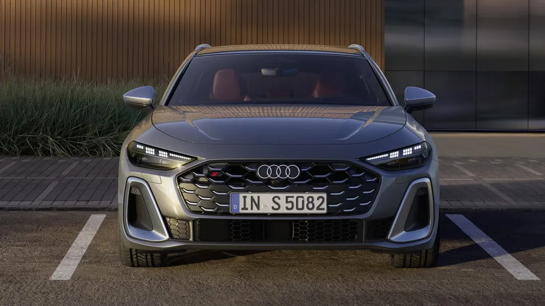 Pohľad na predné partie Audi S5 Avant, ktorý je zaparkovaný pred modernou budovou.