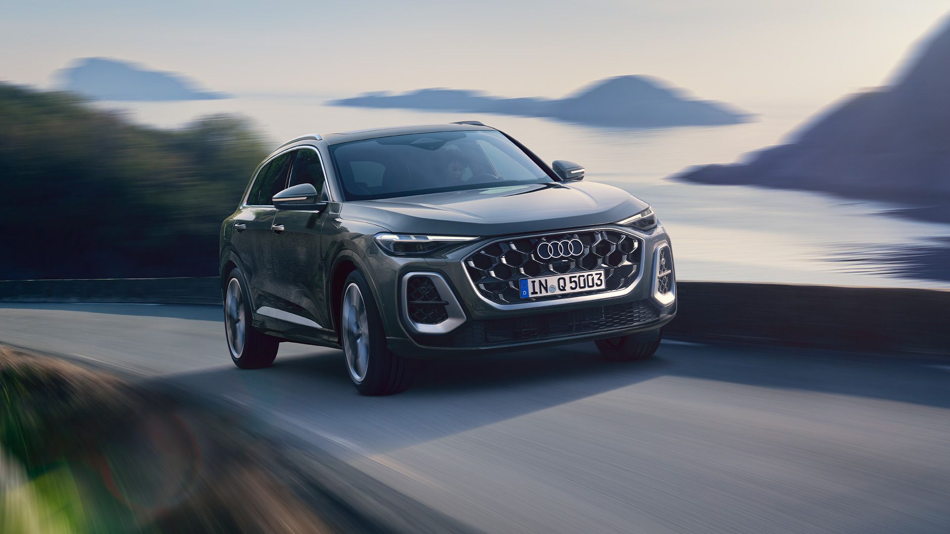 Audi Q5 SUV jazdí po ceste pri pobreží. V pozadí vidieť more, malé ostrovy a pobrežie. Rýchlosť naznačuje rozmazaná krajina.