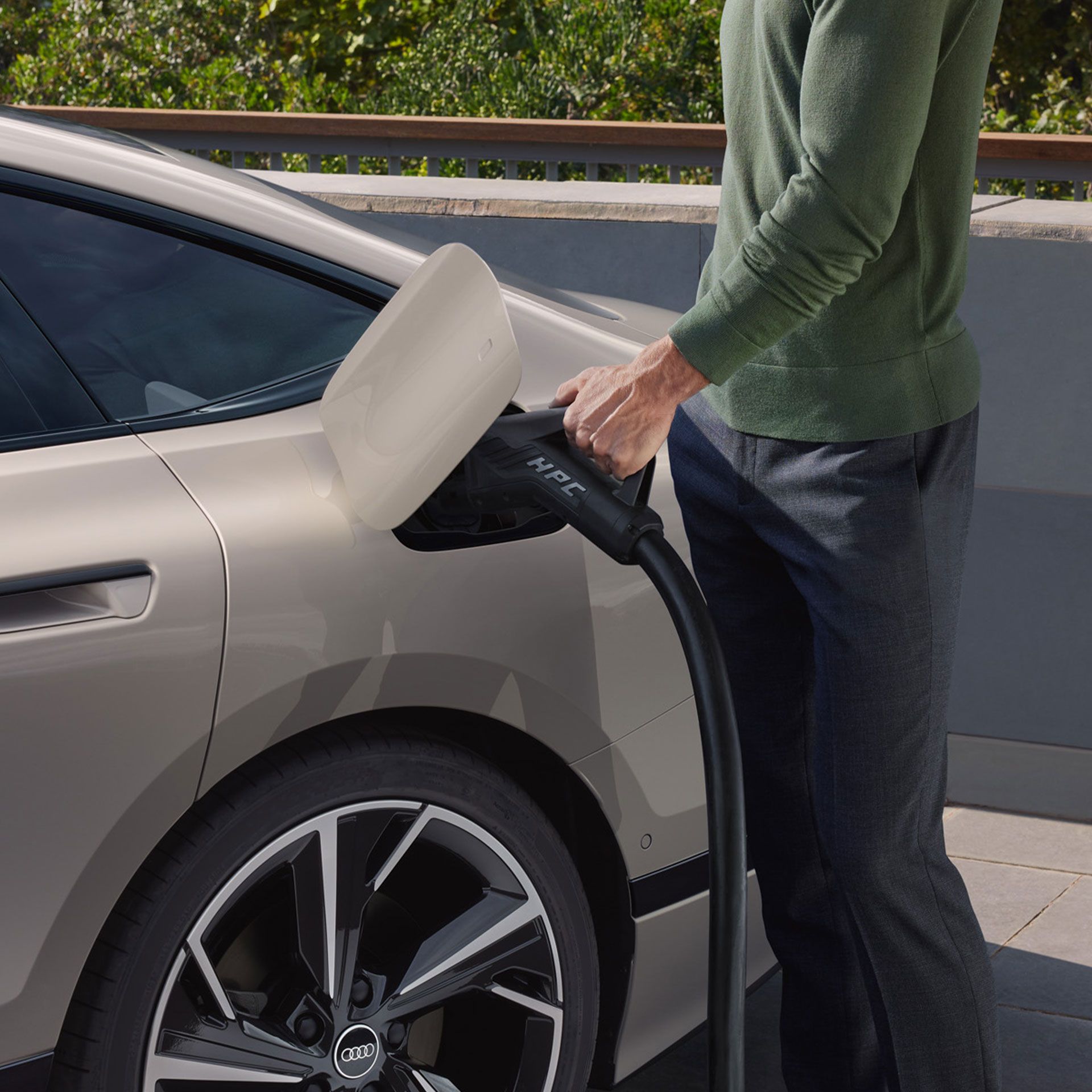 Muž zapája nabíjací kábel pre vysokovýkonné nabíjanie do nabíjacej zásuvky béžového elektrického vozidla značky Audi.