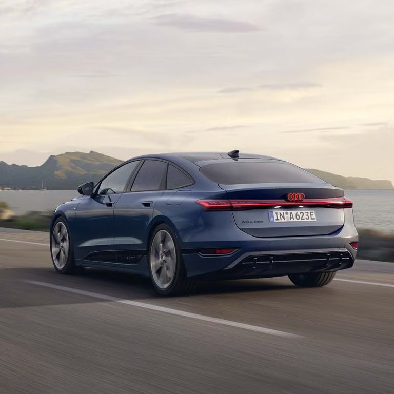 A6 Sportback e-tron, z pohľadu na zadnú časť, jazdí po ceste popri pobreží. V pozadí sú vidieť hory. 