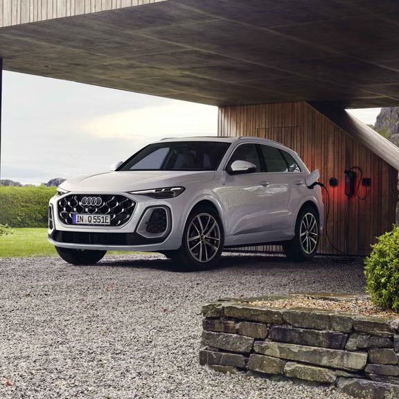 Biele Audi Q5 SUV e-hybrid v šikmom pohľade spredu je pripojený k nabíjacej stanici pod prístreškom pre auto.