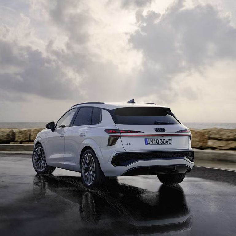 Biele SUV Q3 e-hybrid jazdí po mokrej ceste pozdĺž pobrežia.