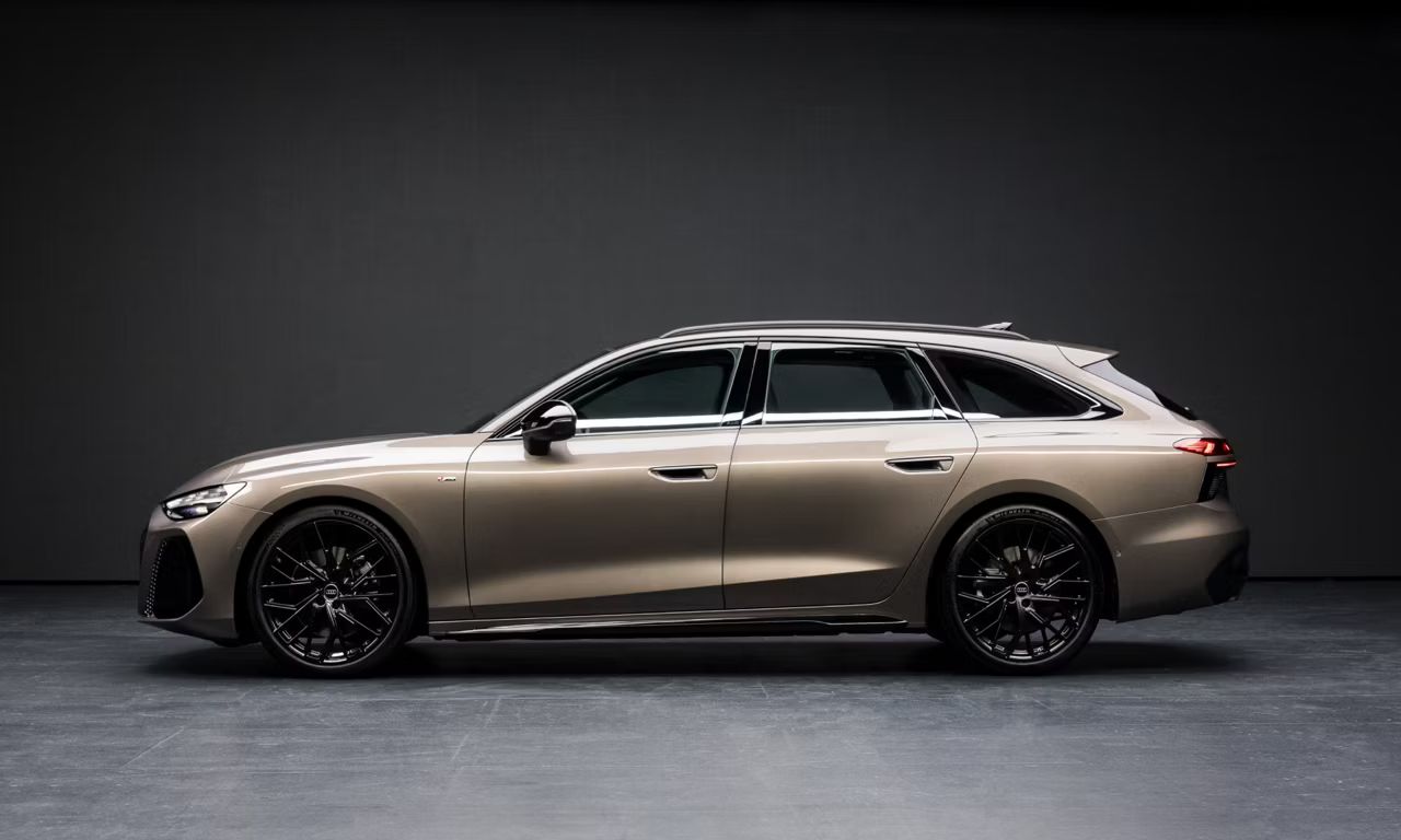 Audi A6 Avant v svetlohnedom metalízovom lakovaní s veľkými čiernymi diskami kolies pred antracitovou stenou. Pohľad zboku. 