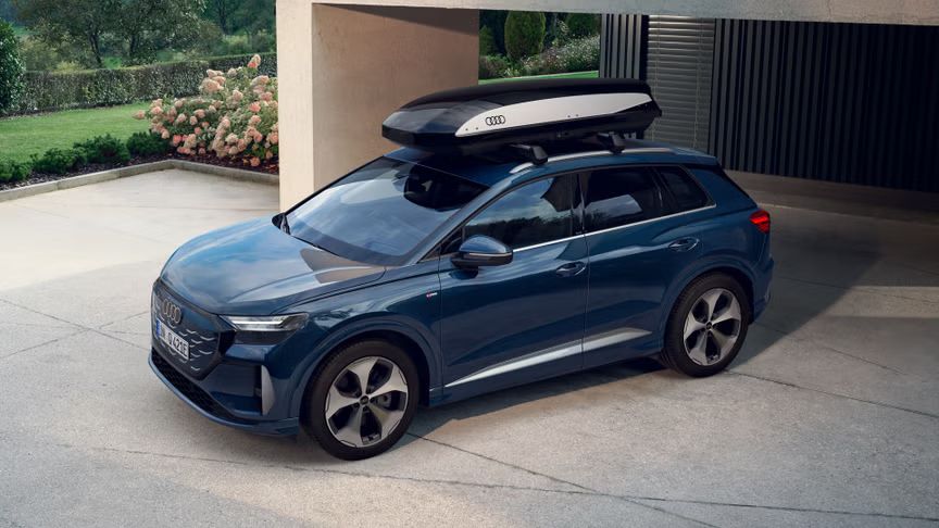 Q4 SUV e-tron so strešným boxom na parkovisku pri modernom dome, v pozadí je upravená záhrada.
