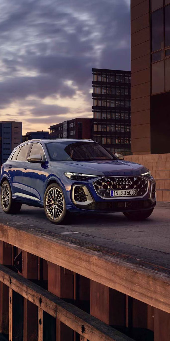 Der SQ5 SUV steht vor der Skyline einer Küstenstadt. Davor befindet sich eine junge, modische Frau. 