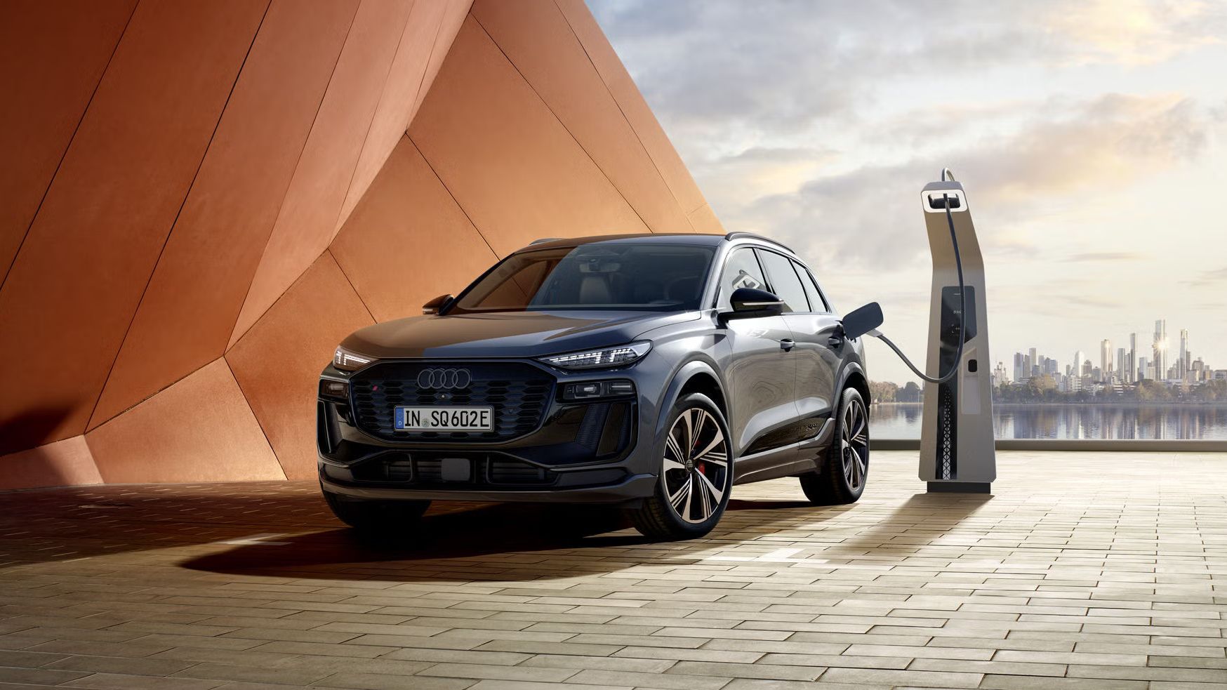 Audi SQ6 SUV e-tron zaparkovaný pri modernej, umeleckej budove a nabíja sa na nabíjacej stanici.