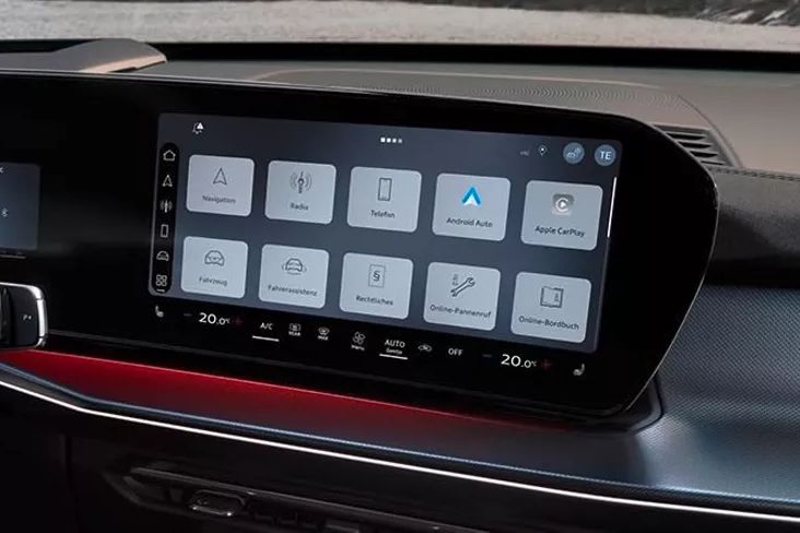 Obrázok zobrazuje interiér Audi Q3 SUV a veľký displej na stredovej konzole. Na displeji sú viditeľné rôzne ovládacie možnosti pre navigáciu, rádio, integráciu smartfónu a funkcie vozidla. Vľavo od displeja je čiastočne viditeľný volant.
